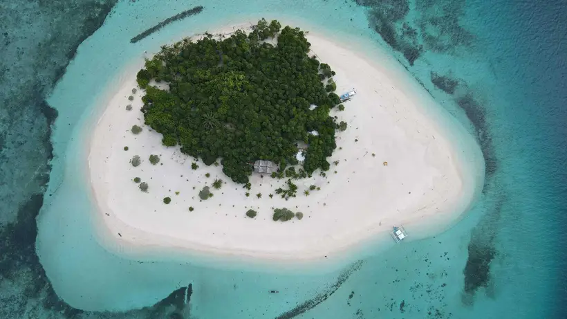 Aerial view of a remote island ringed by a white sandbar and shallow turquoise water