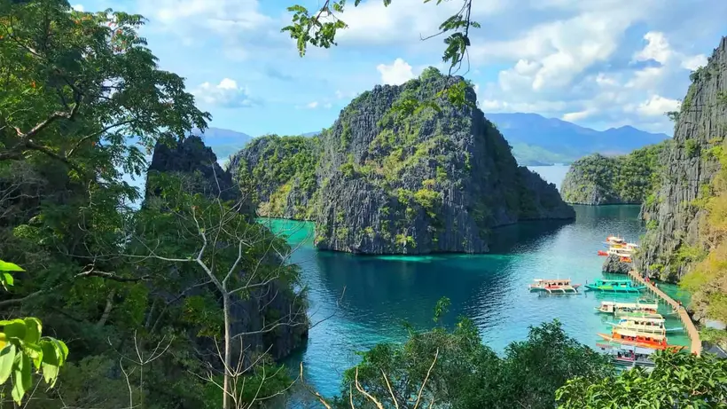 Limestone cliffs above a turquoise lagoon with boats at the shore in Coron