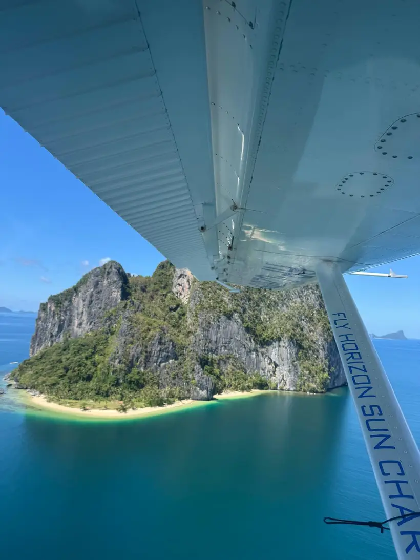 A limestone island and white beach seen past the seaplane's strut