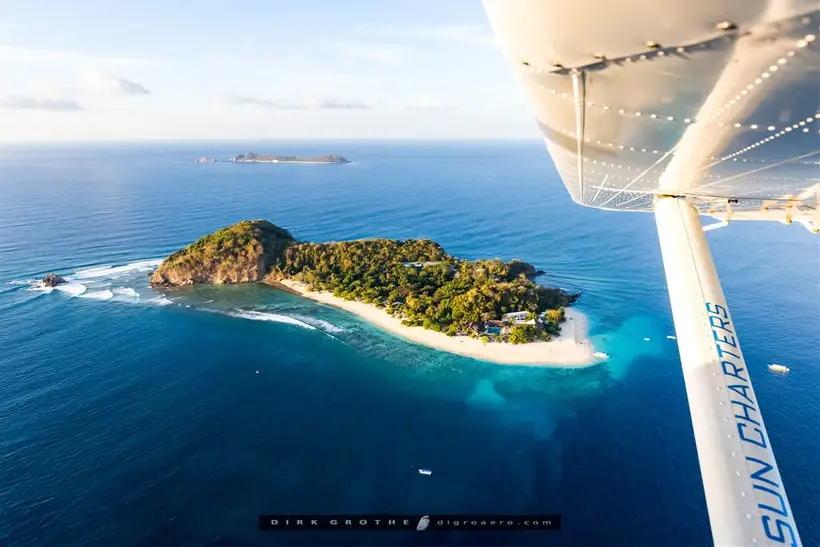 A small wooded island ringed by reef, seen from under the wing