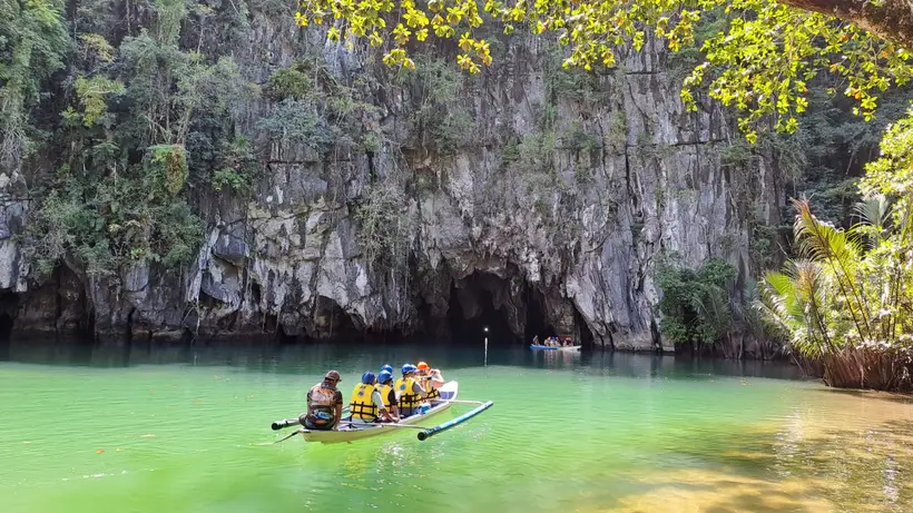 A boat entering a limestone cave over green water in Puerto Princesa